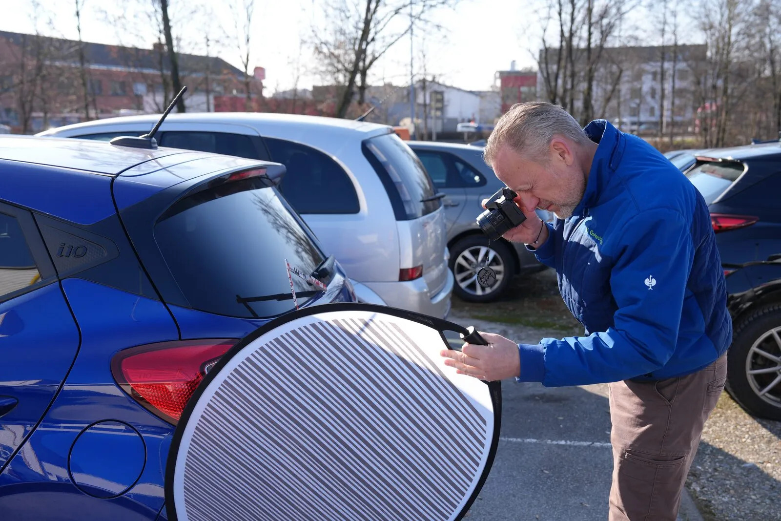 Alexander Ströher prüft mit Kamera und Streifentafel den Lack eines Autos.
